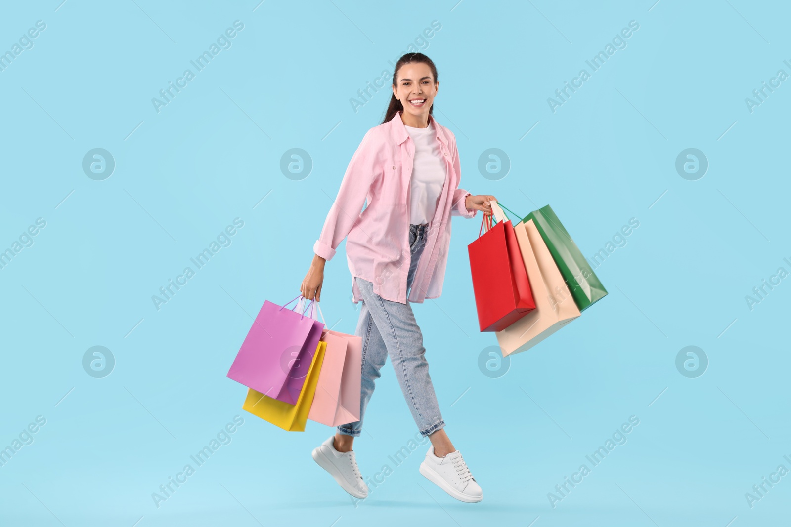 Photo of Smiling woman with colorful shopping bags jumping on light blue background