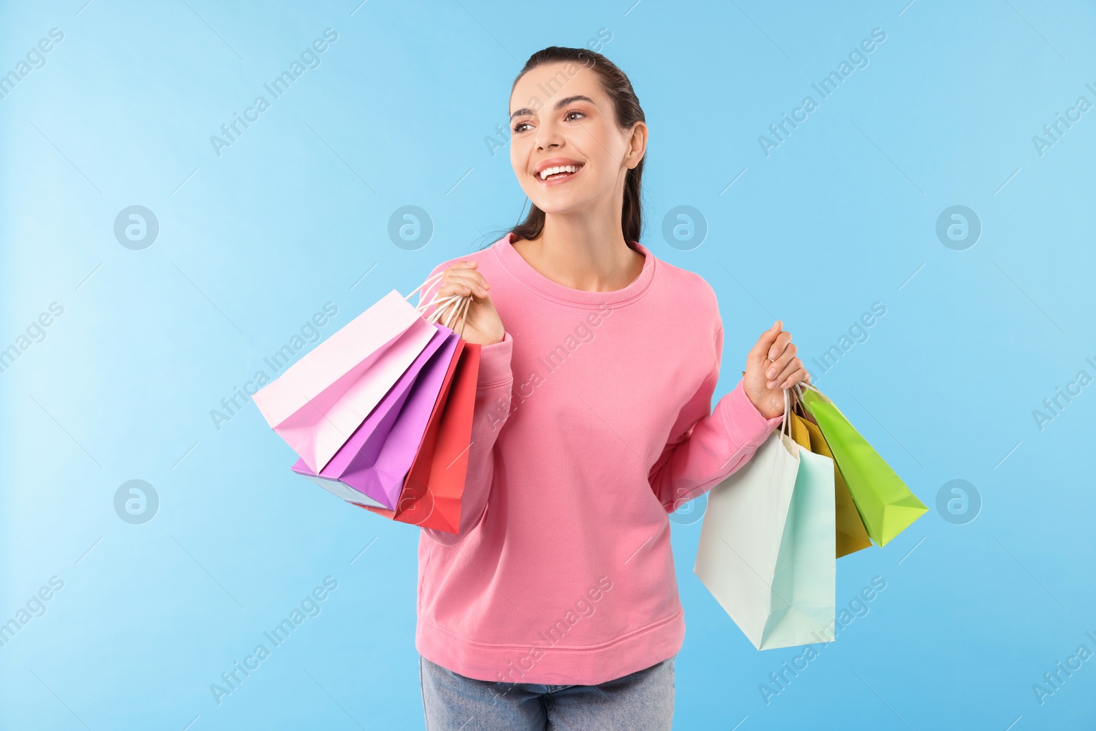 Photo of Smiling woman with colorful shopping bags on light blue background