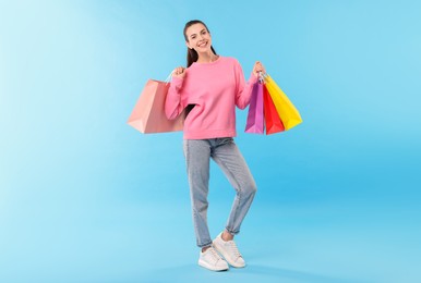 Photo of Smiling woman with colorful shopping bags on light blue background