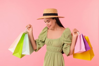 Smiling woman with colorful shopping bags on pink background