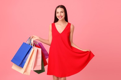 Smiling woman with colorful shopping bags on pink background