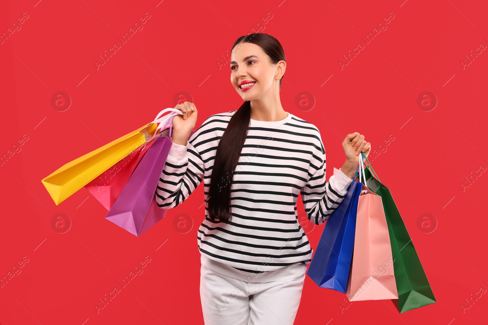 Photo of Smiling woman with colorful shopping bags on red background