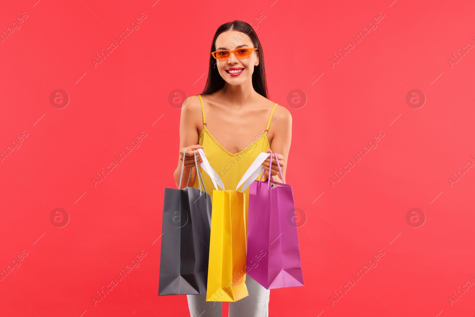 Photo of Smiling woman with colorful shopping bags on red background