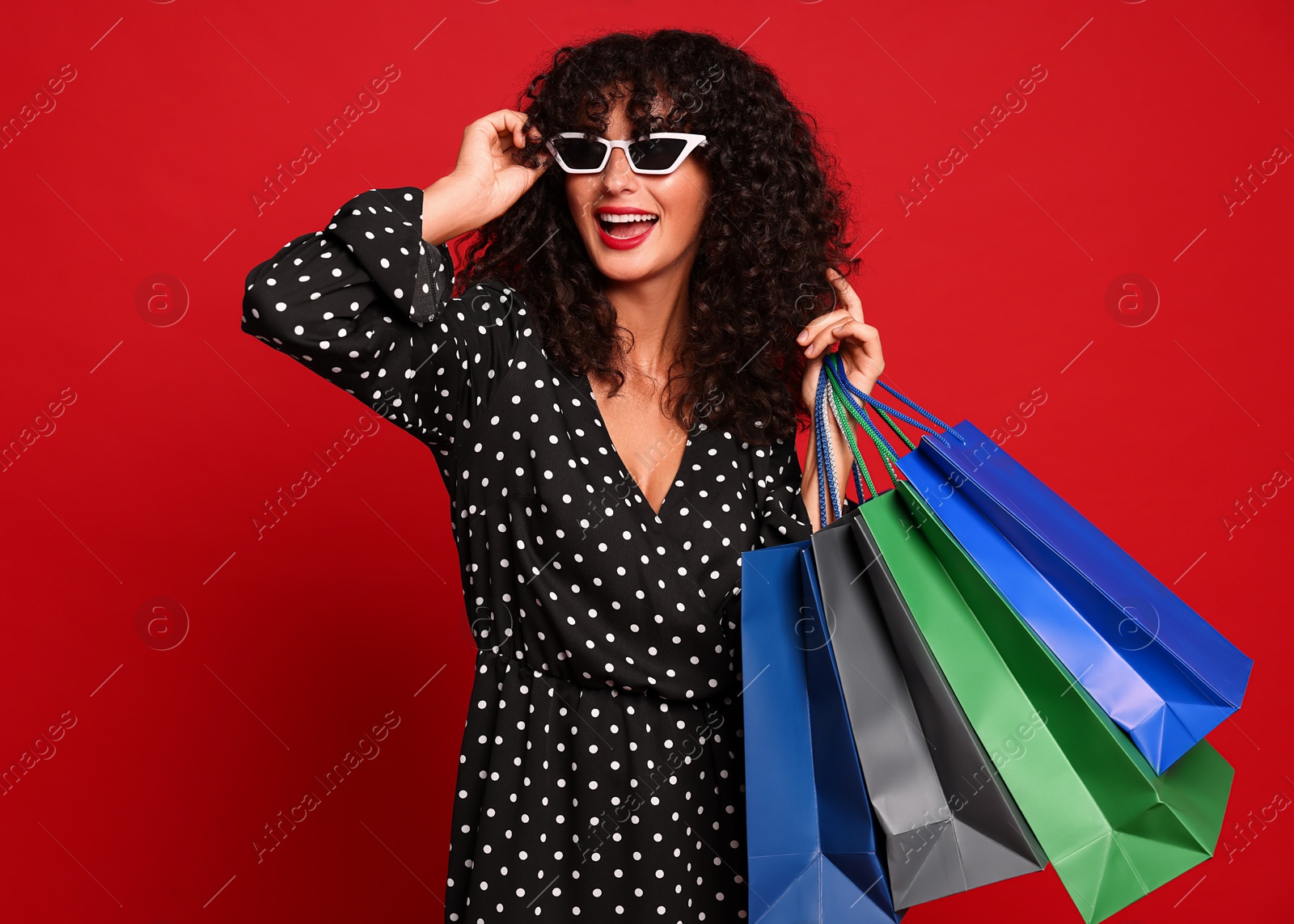 Photo of Happy woman with colorful shopping bags on red background