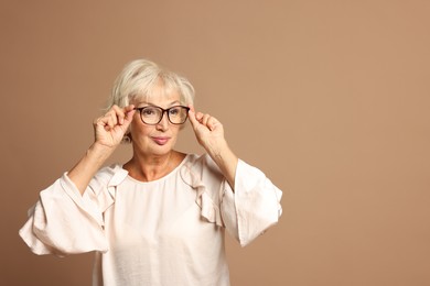 Portrait of beautiful senior woman on light brown background, space for text