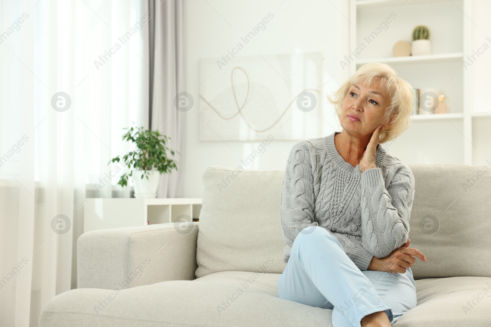 Photo of Beautiful senior woman sitting on sofa at home, space for text