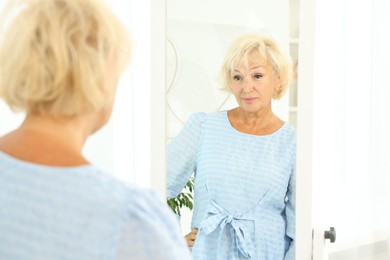 Beautiful senior woman near mirror at home