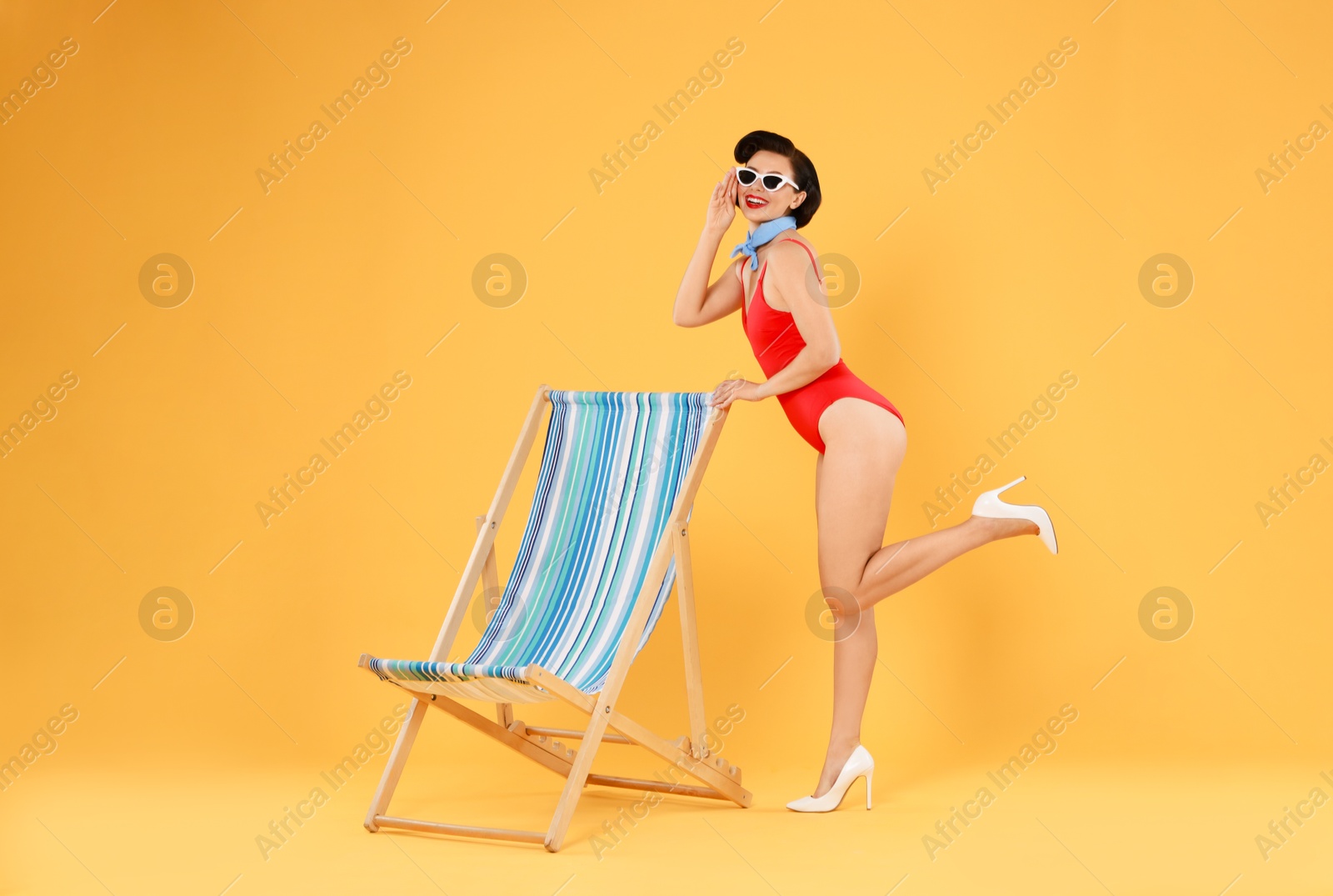 Photo of Pin-up woman in swimsuit near folding chair on orange background