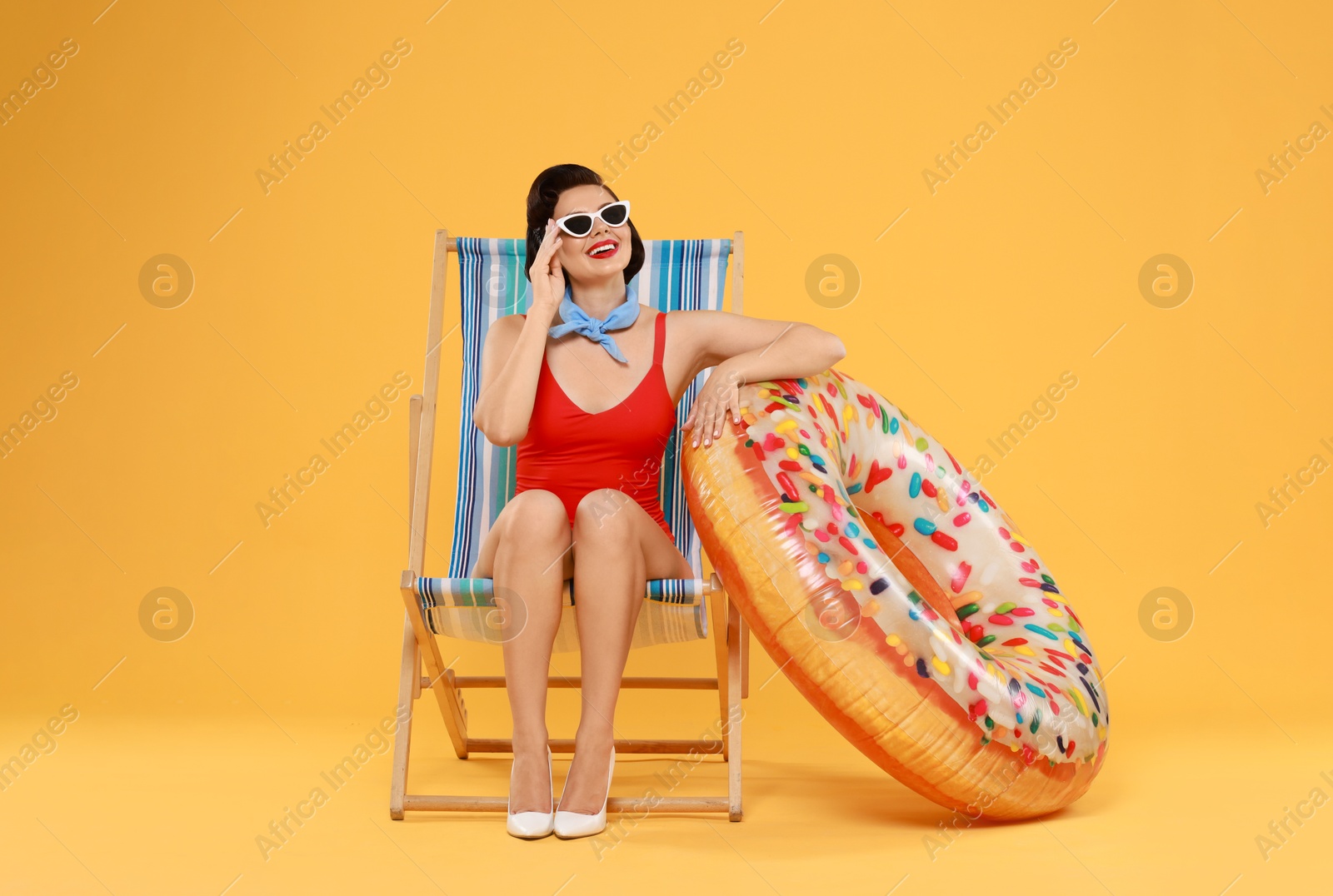 Photo of Pin-up woman in swimsuit with inflatable ring on folding chair against orange background