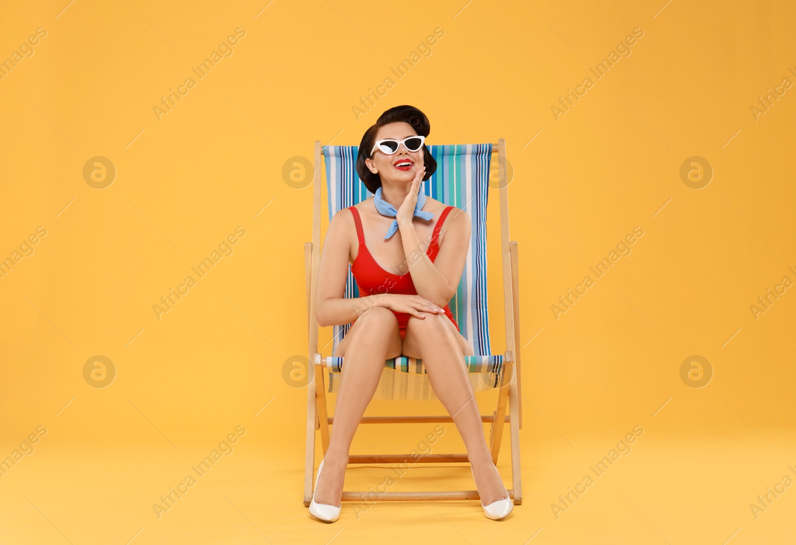 Photo of Pin-up woman in swimsuit on folding chair against orange background