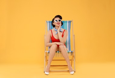 Pin-up woman in swimsuit on folding chair against orange background