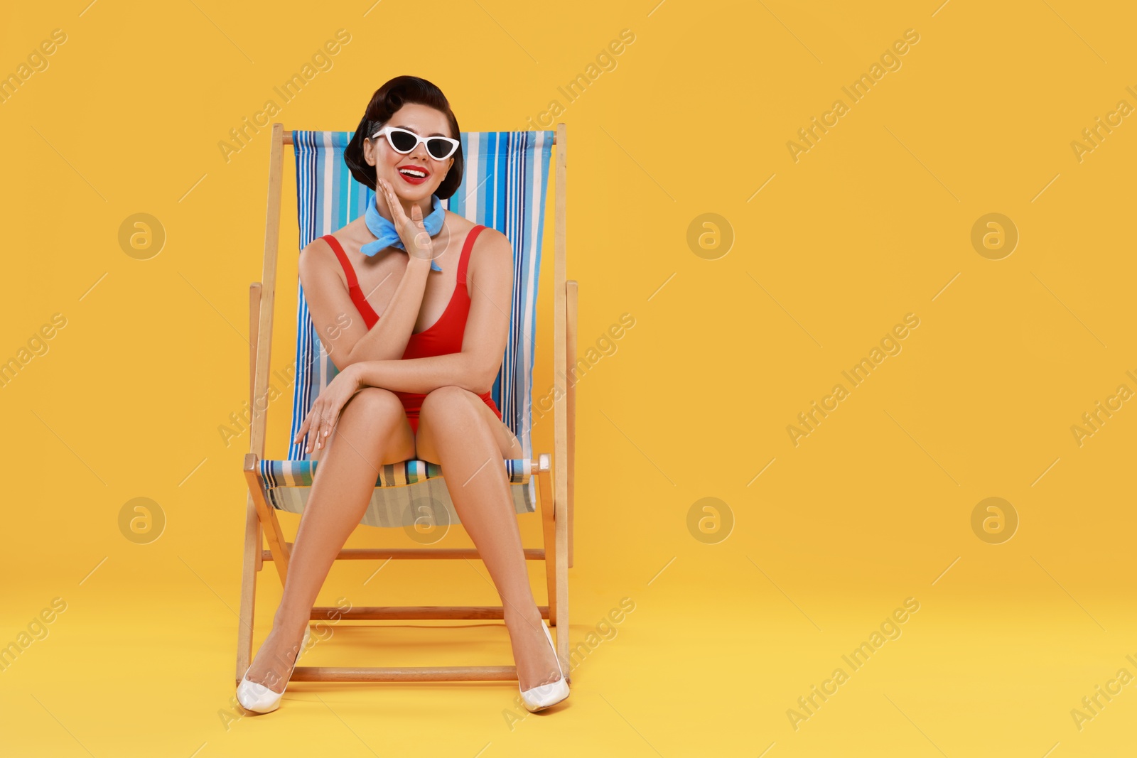 Photo of Pin-up woman in swimsuit on folding chair against orange background, space for text