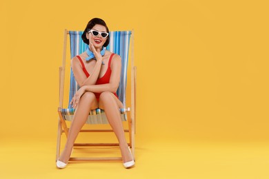 Pin-up woman in swimsuit on folding chair against orange background, space for text