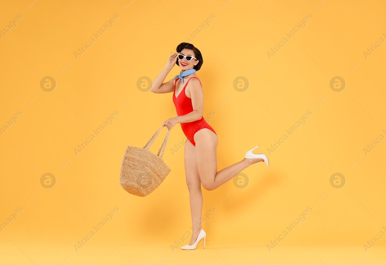 Photo of Pin-up woman in swimsuit with beach bag on orange background