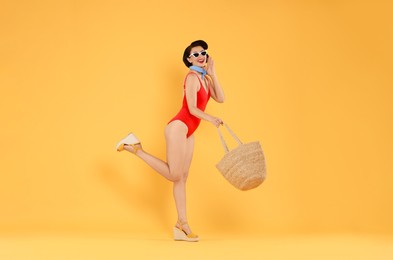 Photo of Pin-up woman in swimsuit with beach bag on orange background