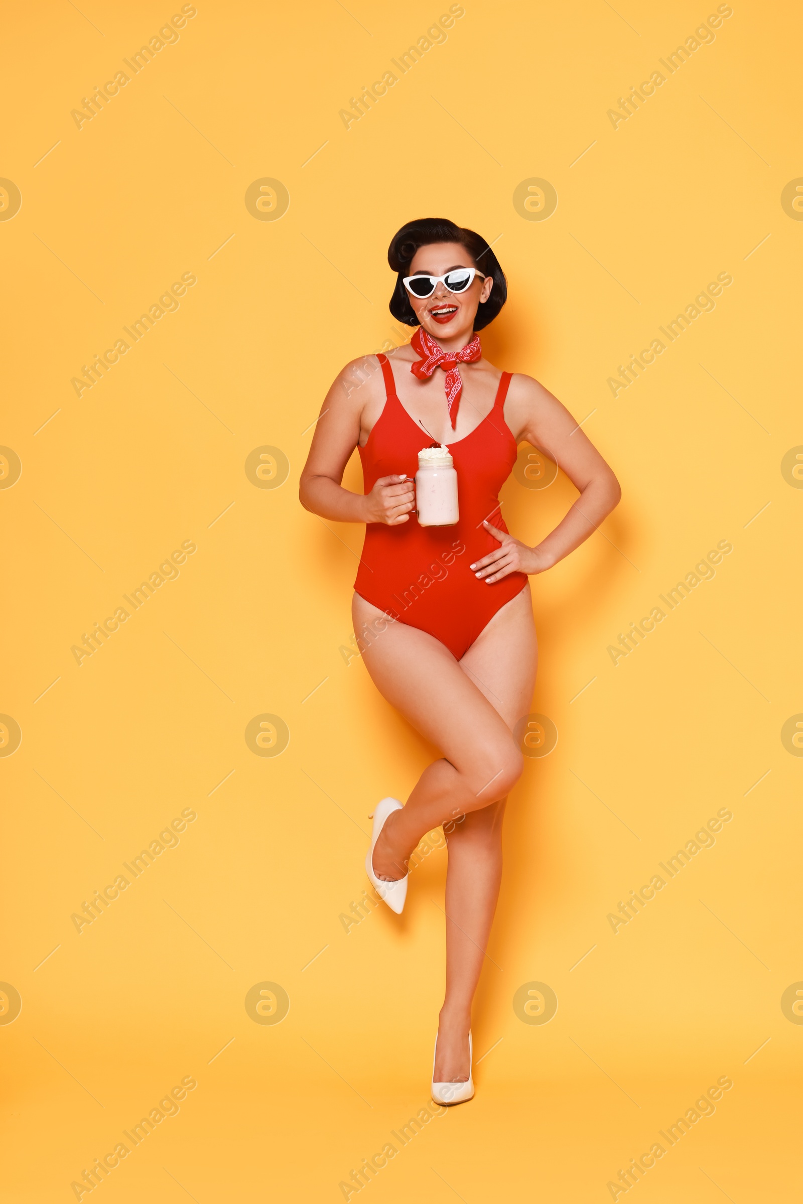 Photo of Pin-up woman in swimsuit with milk shake on orange background