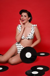 Pin-up woman in bikini with vinyl records on red background