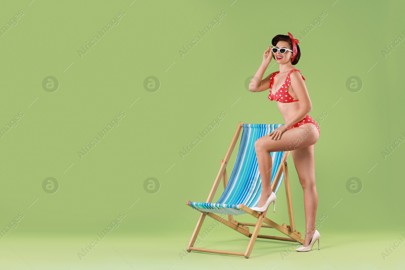 Photo of Pin-up woman in bikini near folding chair on green background, space for text