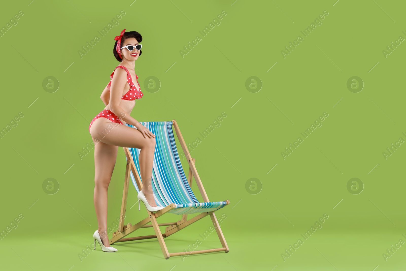 Photo of Pin-up woman in bikini near folding chair on green background, space for text