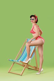 Pin-up woman in bikini near folding chair on green background