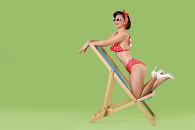 Photo of Pin-up woman in bikini on folding chair against green background, space for text