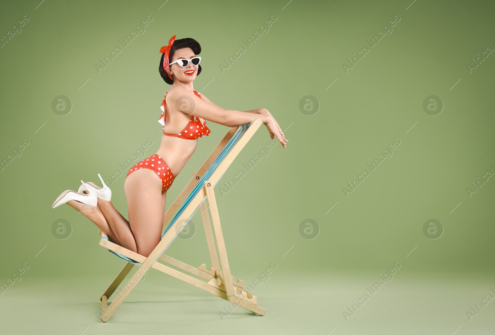 Photo of Pin-up woman in bikini on folding chair against green background, space for text