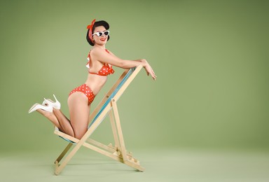 Pin-up woman in bikini on folding chair against green background, space for text