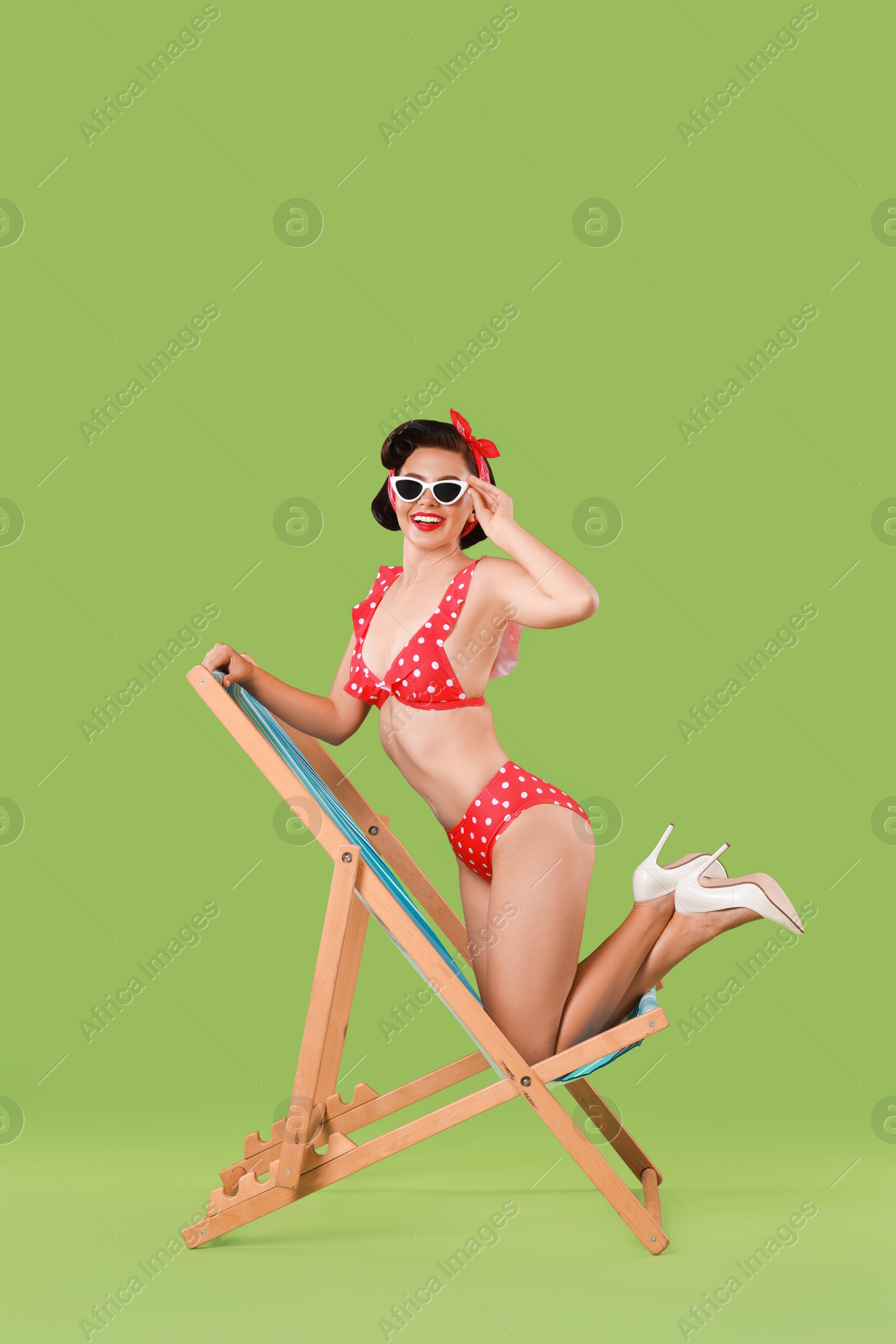 Photo of Pin-up woman in bikini on folding chair against green background