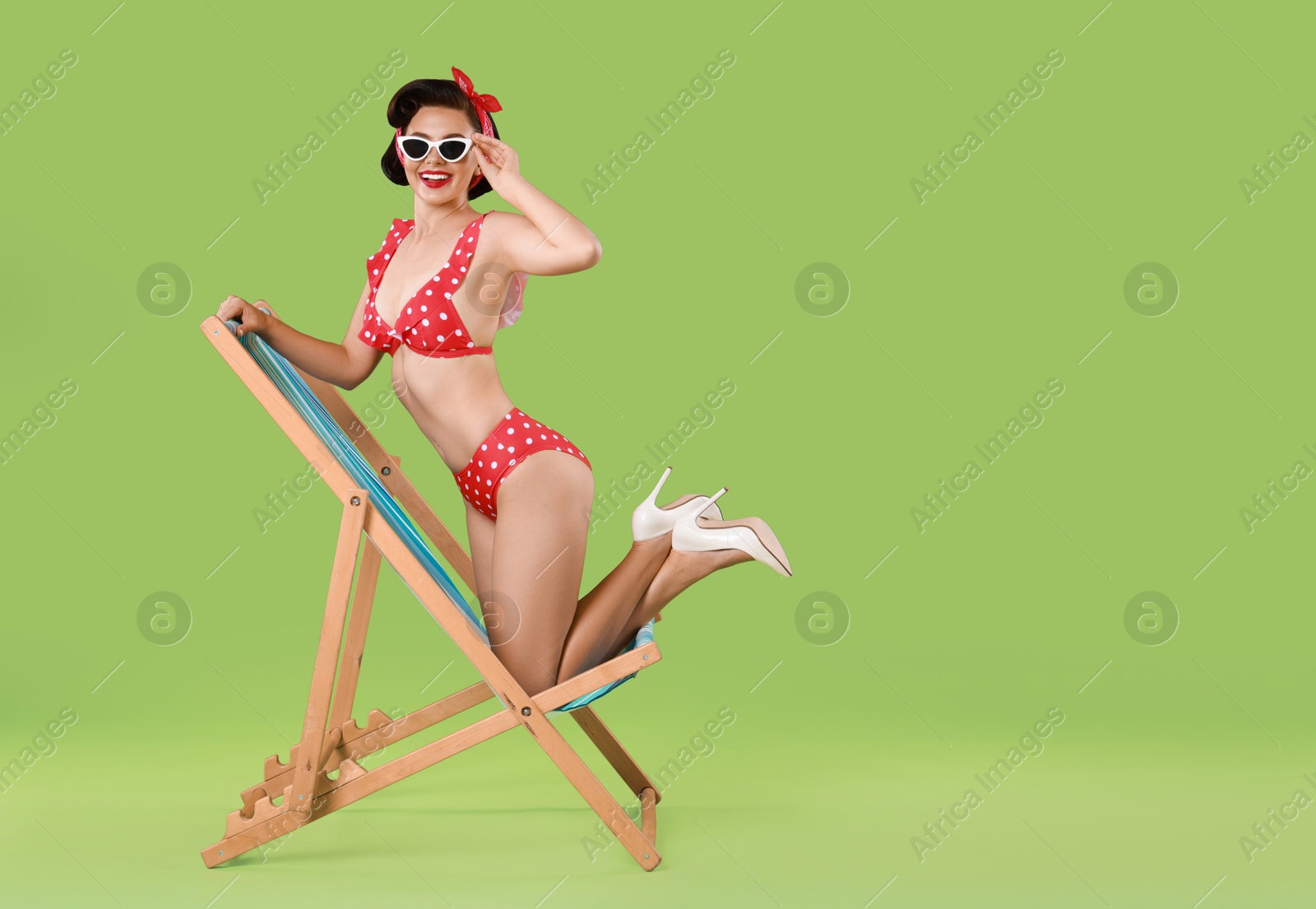 Photo of Pin-up woman in bikini on folding chair against green background, space for text