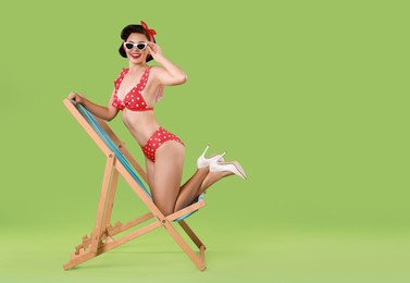 Pin-up woman in bikini on folding chair against green background, space for text