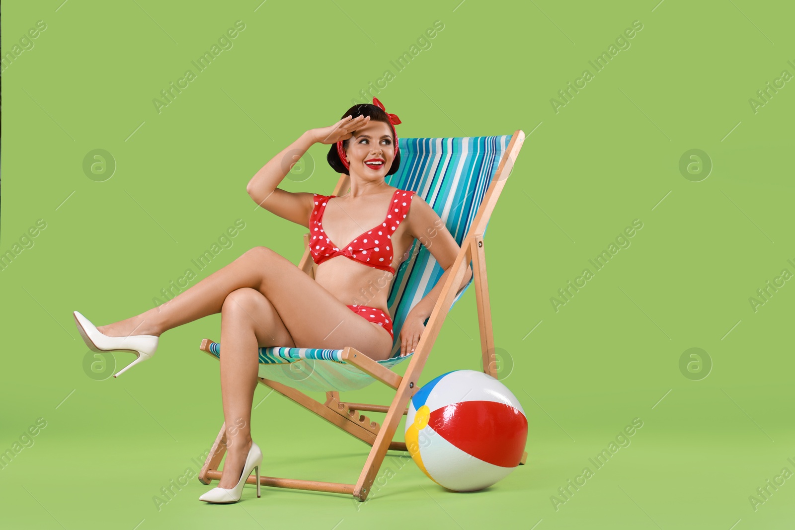 Photo of Pin-up woman in bikini on folding chair against green background, space for text