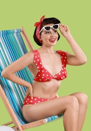 Pin-up woman in bikini on folding chair against green background