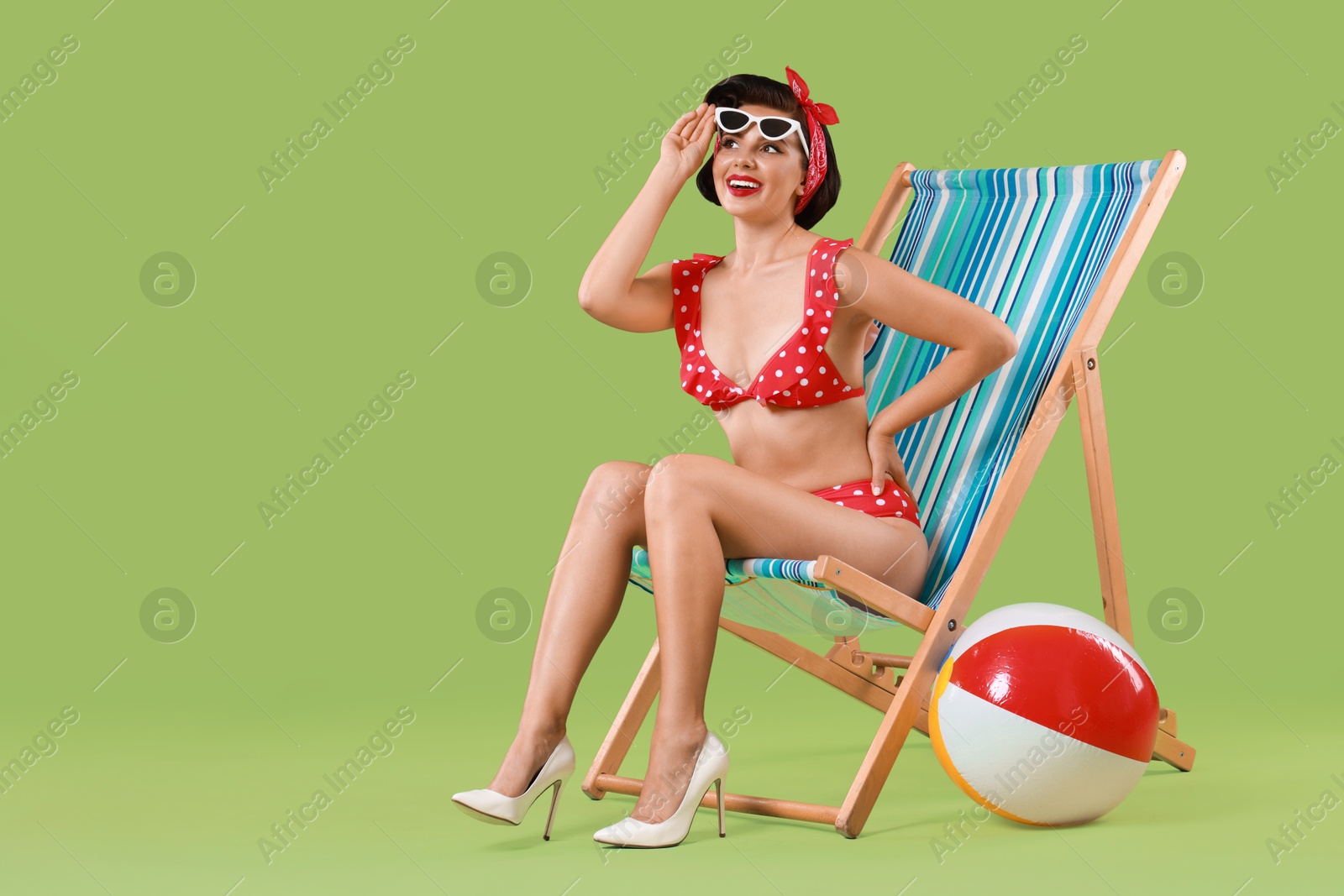 Photo of Pin-up woman in bikini on folding chair against green background, space for text