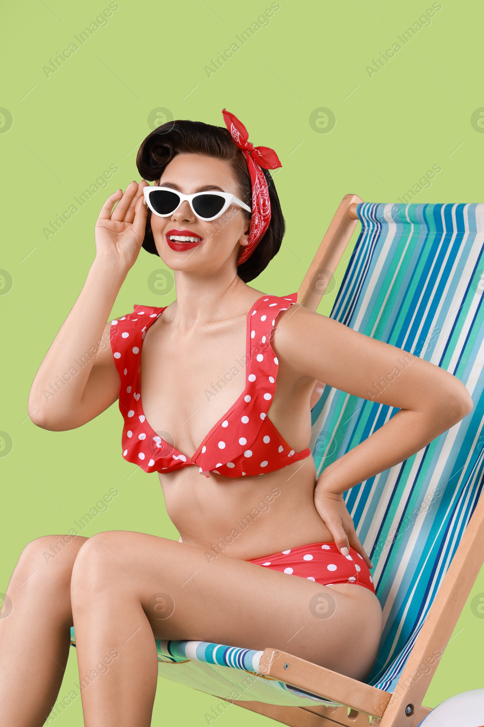 Photo of Pin-up woman in bikini on folding chair against green background