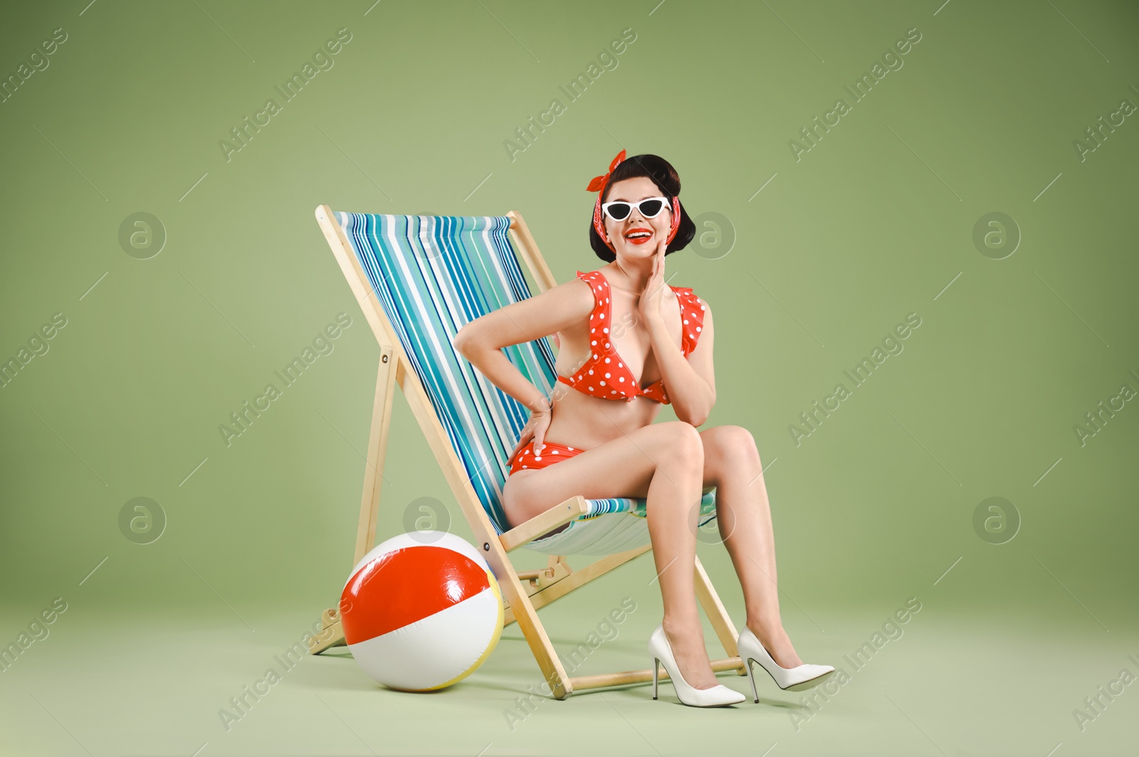 Photo of Pin-up woman in bikini on folding chair against green background