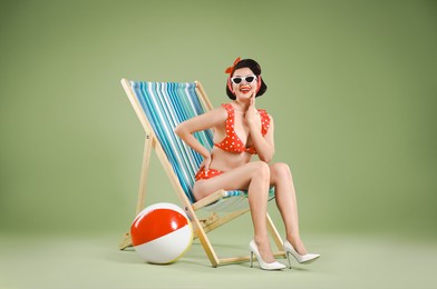 Pin-up woman in bikini on folding chair against green background