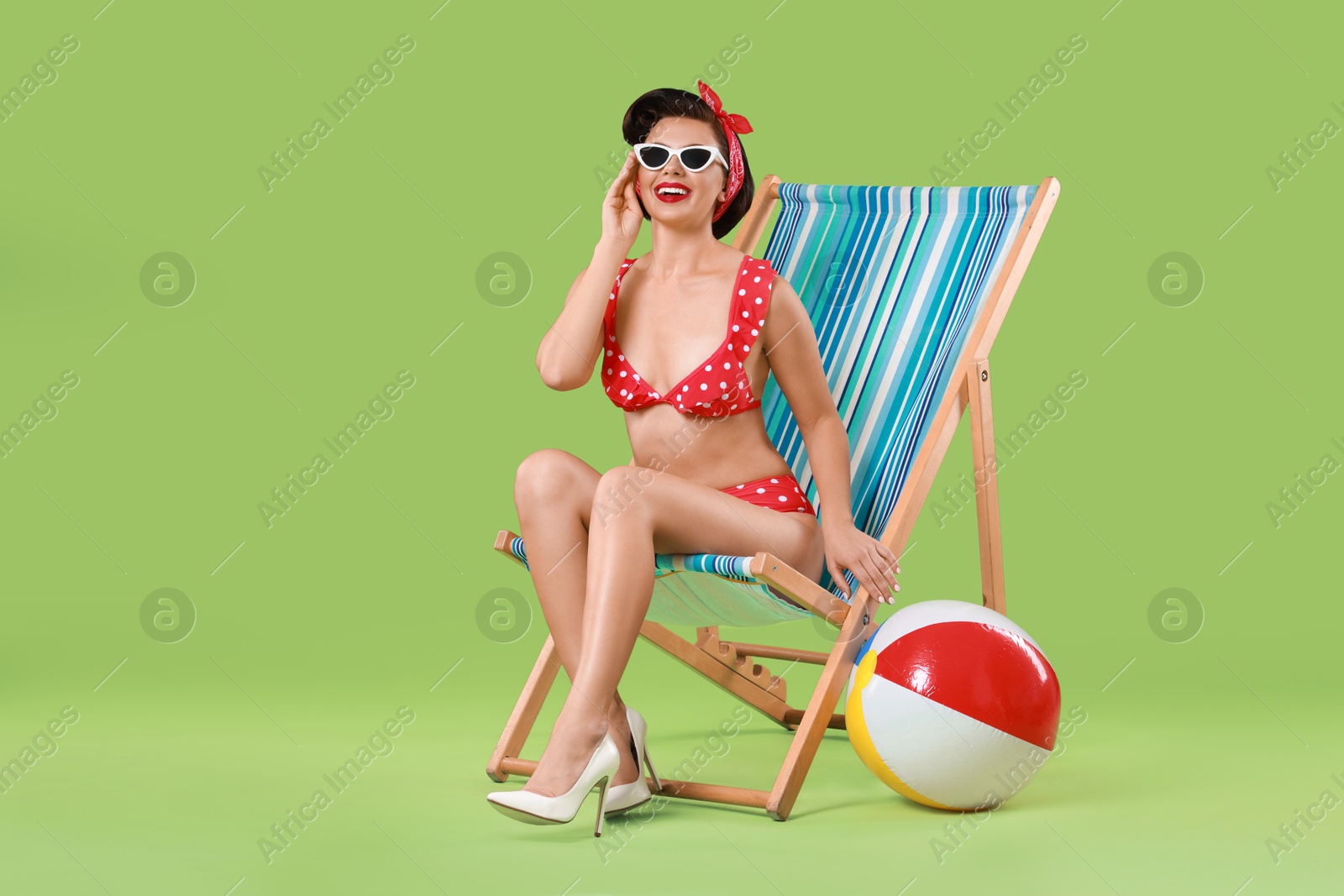 Photo of Pin-up woman in bikini on folding chair against green background