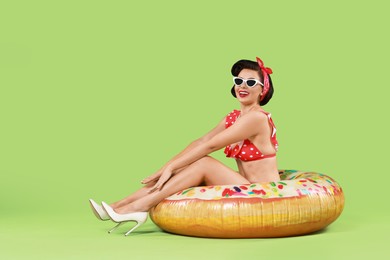 Photo of Pin-up woman in bikini with inflatable ring on green background