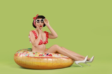 Pin-up woman in bikini with inflatable ring on green background