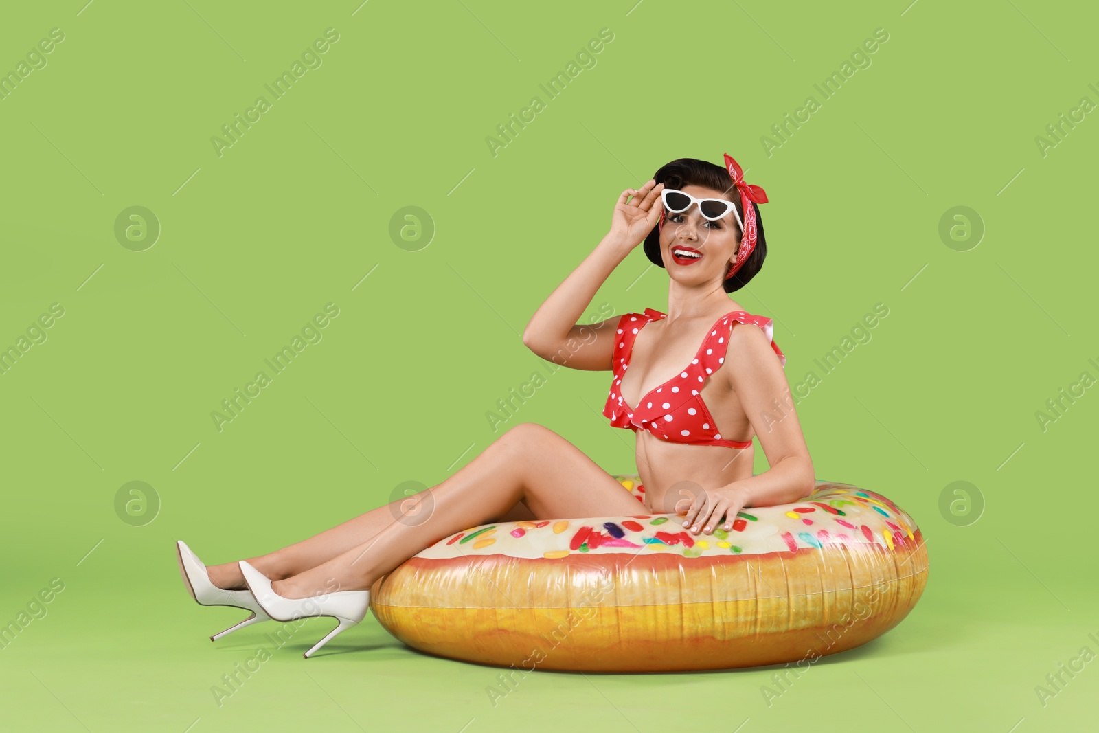 Photo of Pin-up woman in bikini with inflatable ring on green background