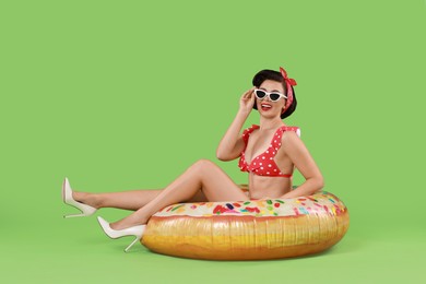 Pin-up woman in bikini with inflatable ring on green background