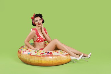 Pin-up woman in bikini with inflatable ring on green background