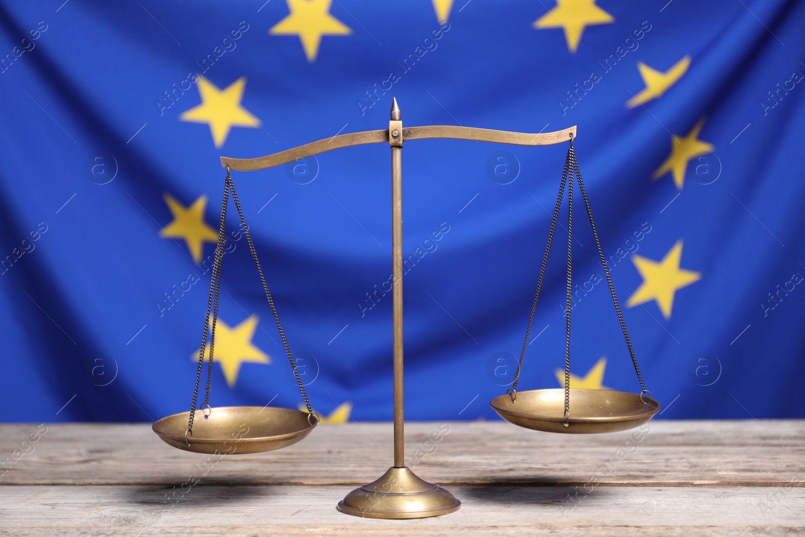 Photo of Scales of justice on wooden table against European Union flag