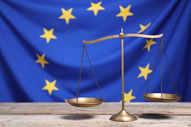 Scales of justice on wooden table against European Union flag, space for text