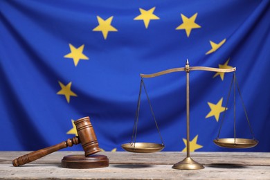 Scales of justice and judge's gavel on wooden table against European Union flag