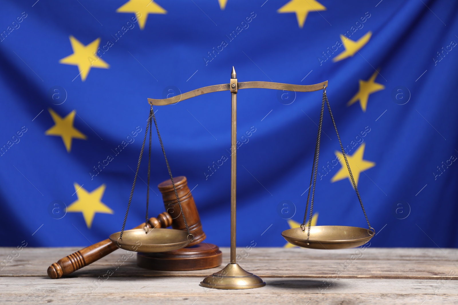 Photo of Scales of justice and judge's gavel on wooden table against European Union flag