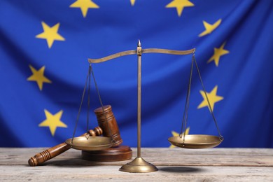 Photo of Scales of justice and judge's gavel on wooden table against European Union flag