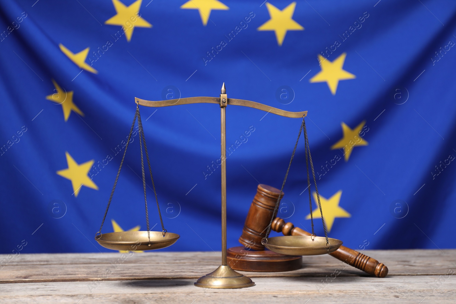 Photo of Scales of justice and judge's gavel on wooden table against European Union flag