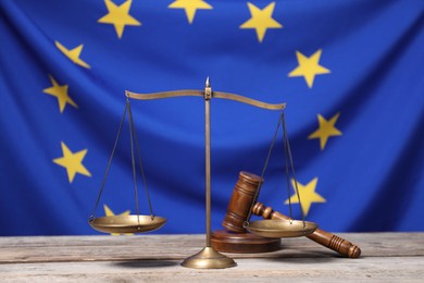 Scales of justice and judge's gavel on wooden table against European Union flag