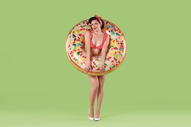 Pin-up woman in bikini with inflatable ring on green background